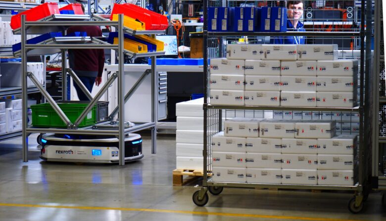 A Bosch Rexroth autonomous mobile robot (AMR) carrying a pick cart inside a warehouse and surrounded by other carts.