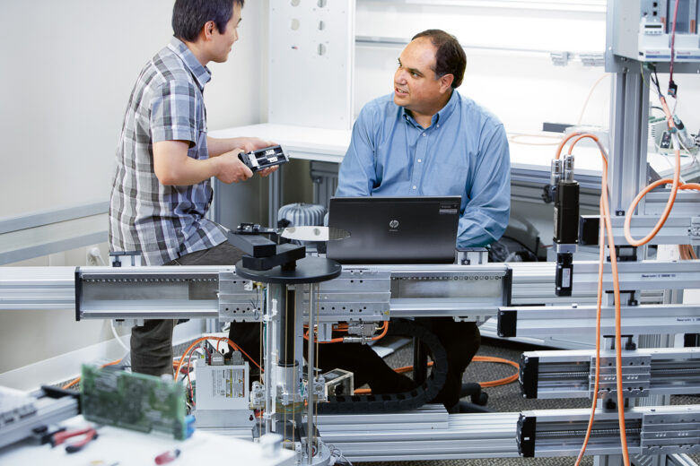 Two engineers having a conversation behind semiconductor automation system equipment from Bosch Rexroth.