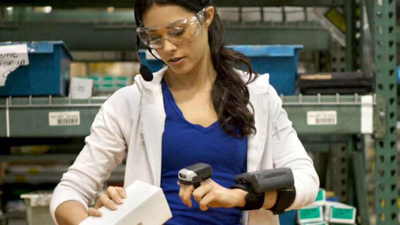 A warehouse worker using a wearable device with AI-embedded technology to scan an inventory item.