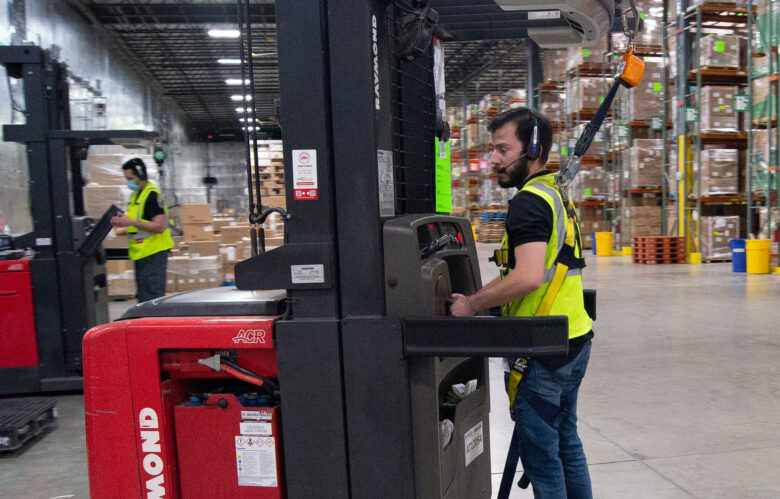 A warehouse worker wears AI-embedded technology and a headset while operating a forklift.