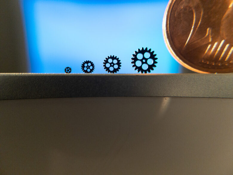 Four micro additively manufactured gears in a row compared to a coin.